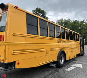 Yellow Freightliner Thomas B2B/C2 school bus side view with black-tinted windows and ‘Lansing Central’ lettering, cargo doors closed, in a parking lot.