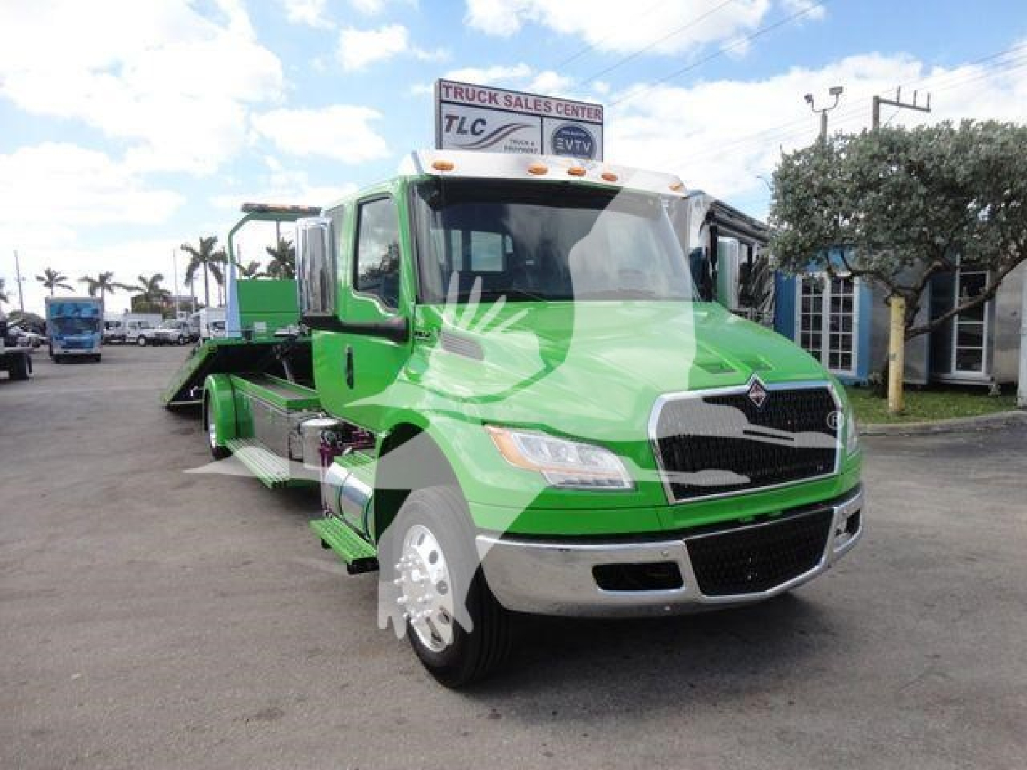 Truck bay showing a green 2027 International MV tow/rollback truck with chrome grille and black front bumper in a dealership lot.