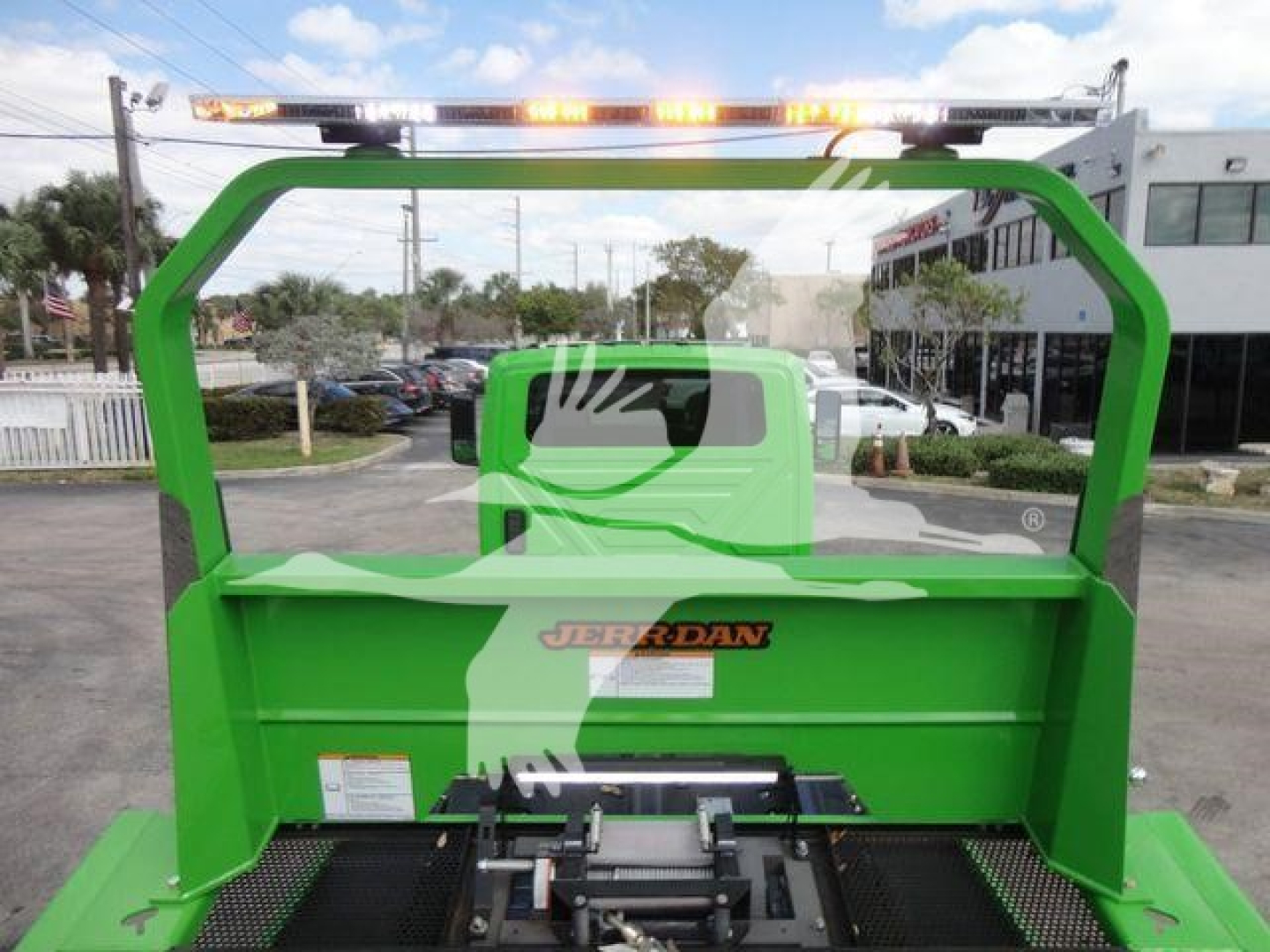 Green Jordan rollback with overhead beacon lights and logo bumper showing hydraulic components and rear bed.