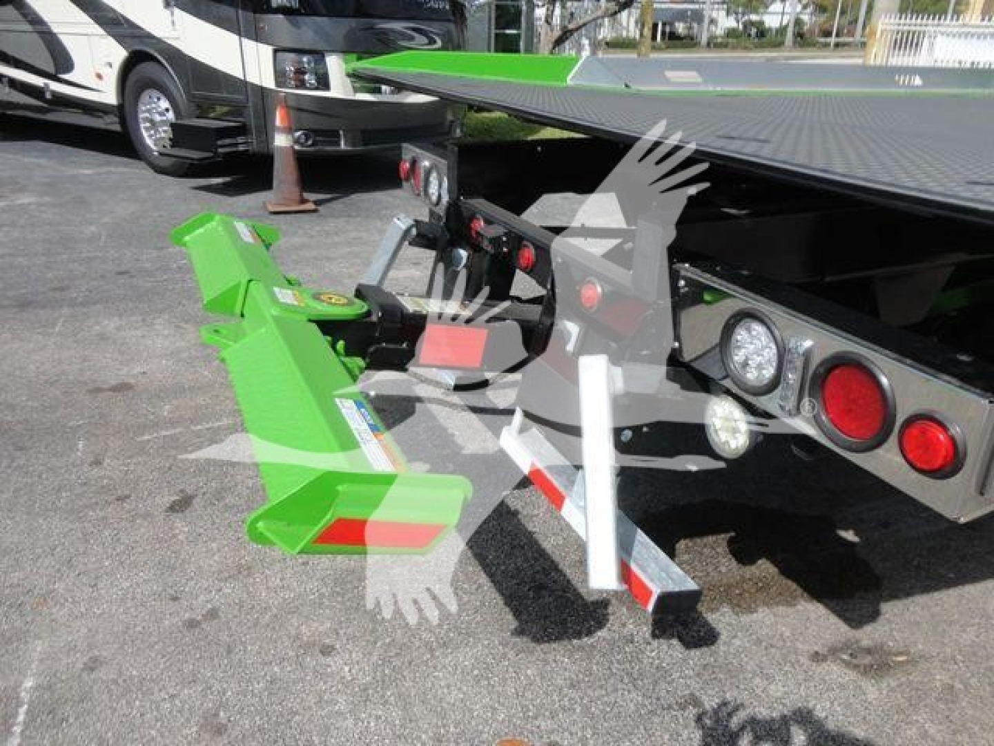 Green tow hitch/loader attachment mounted on a truck bed with hydraulic arms and safety reflectors visible.