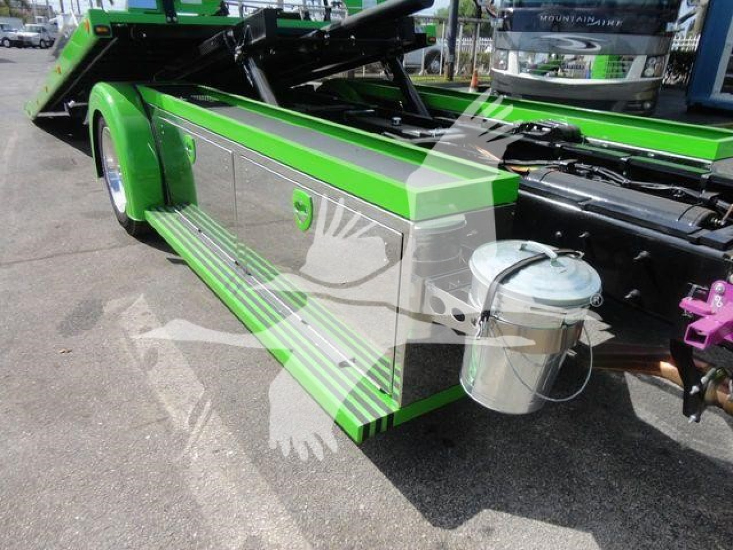 Truck bed side step with green and silver color, hydraulic rollback equipment, cylindrical aluminum reservoir, and chrome accents.