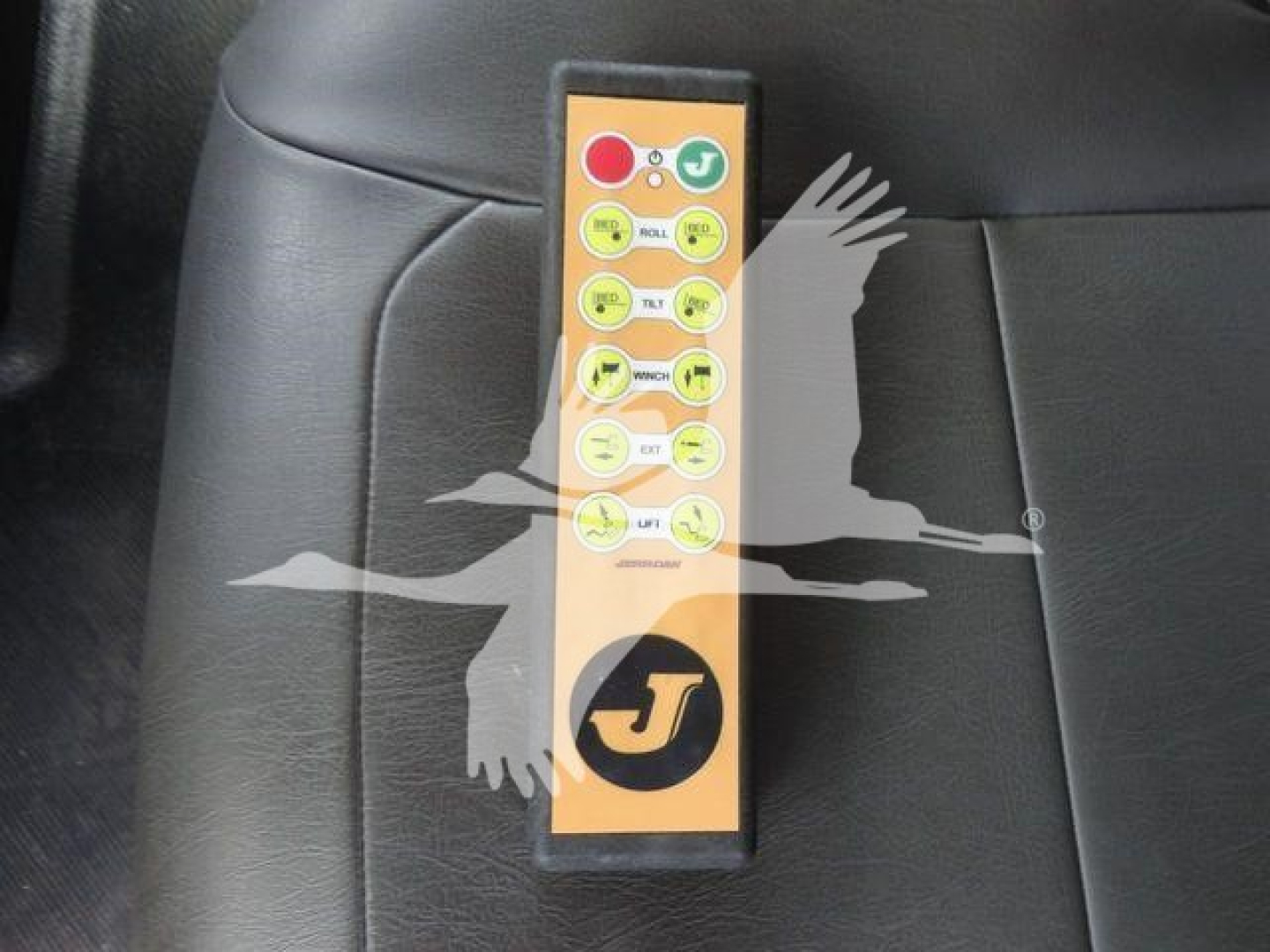 Panel with multiple round yellow buttons and red stop button on a black seat back, with a J logo at bottom; appears to be a control remote in a vehicle interior.
