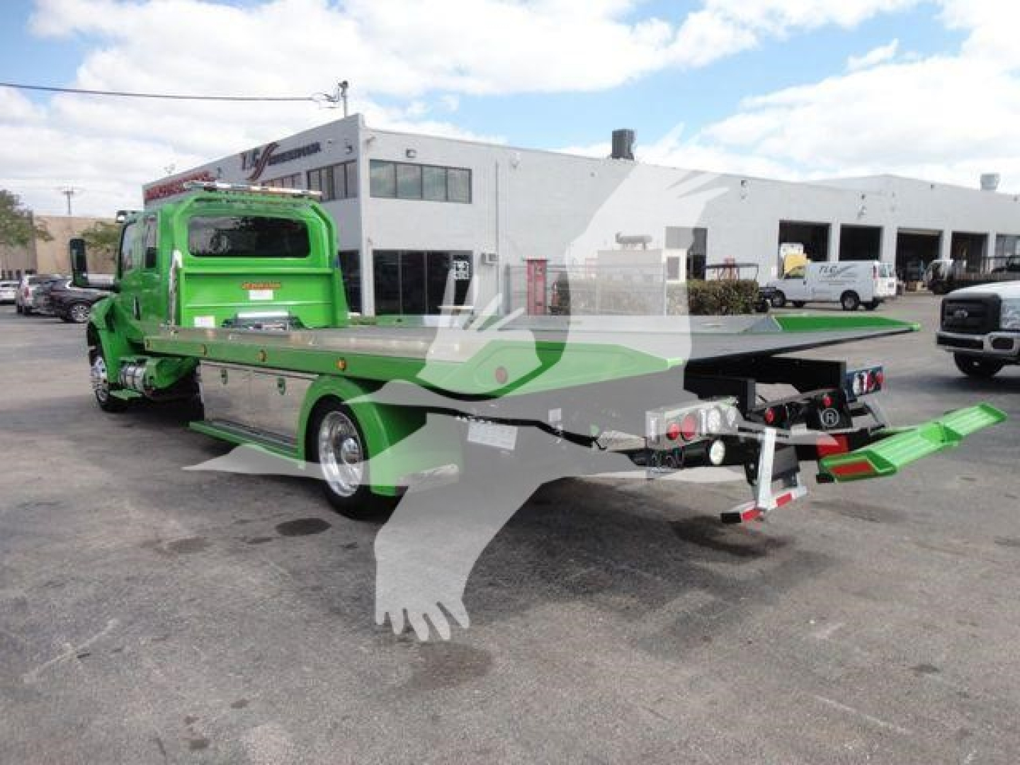 Green International MV tow truck with flatbed in a dealership lot, side view showing rollback configuration and loading ramps.