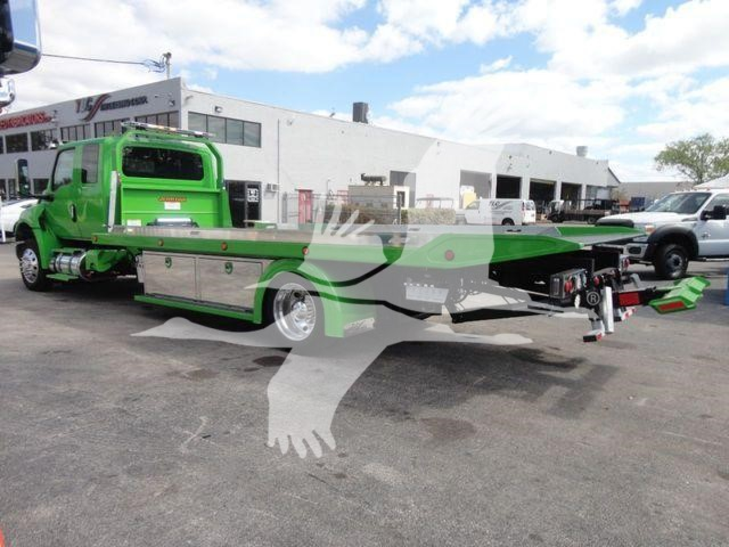 Green International tow truck with flatbed in a dealership lot, MV607STEPSIDEFM stock number visible; rollback category, new truck.