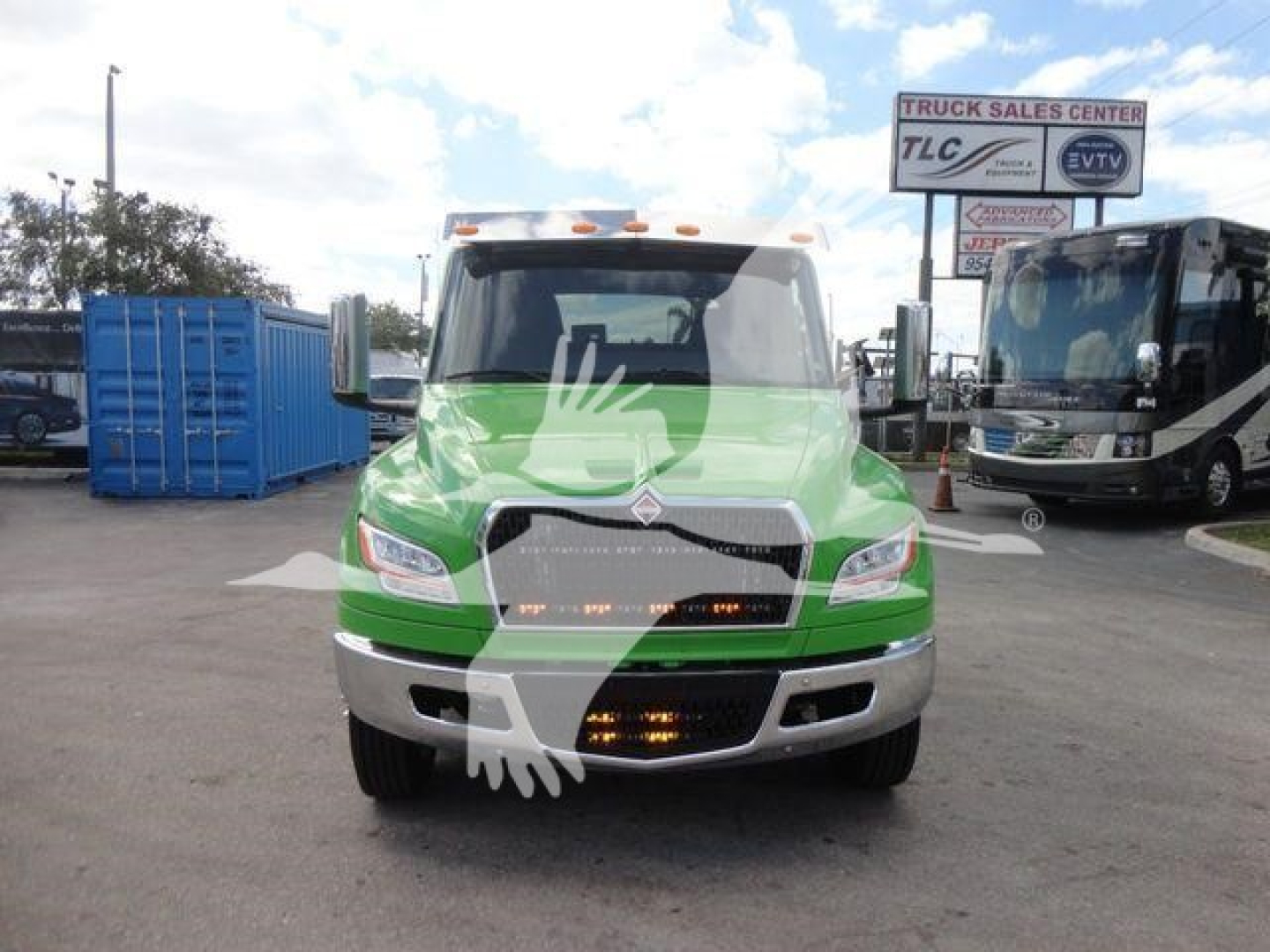 Front view of a green 2027 International MV rollback truck with chrome bumper, daytime running lights, and dealership signs in the background.
