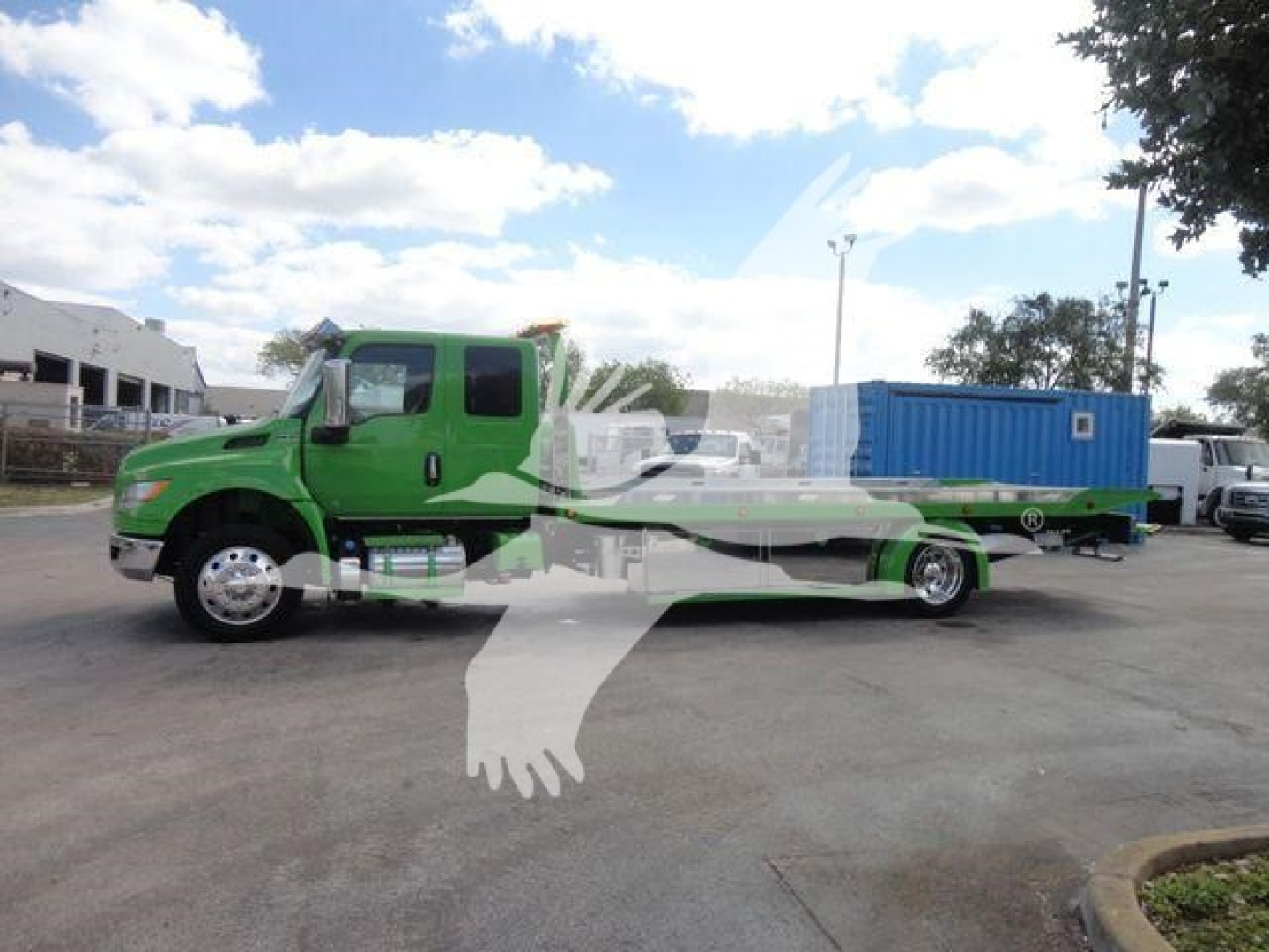 2027 International MV rollback tow truck with a bright green cab and a long flatbed, displaying a blue container on the bed; clear sky with scattered clouds.
