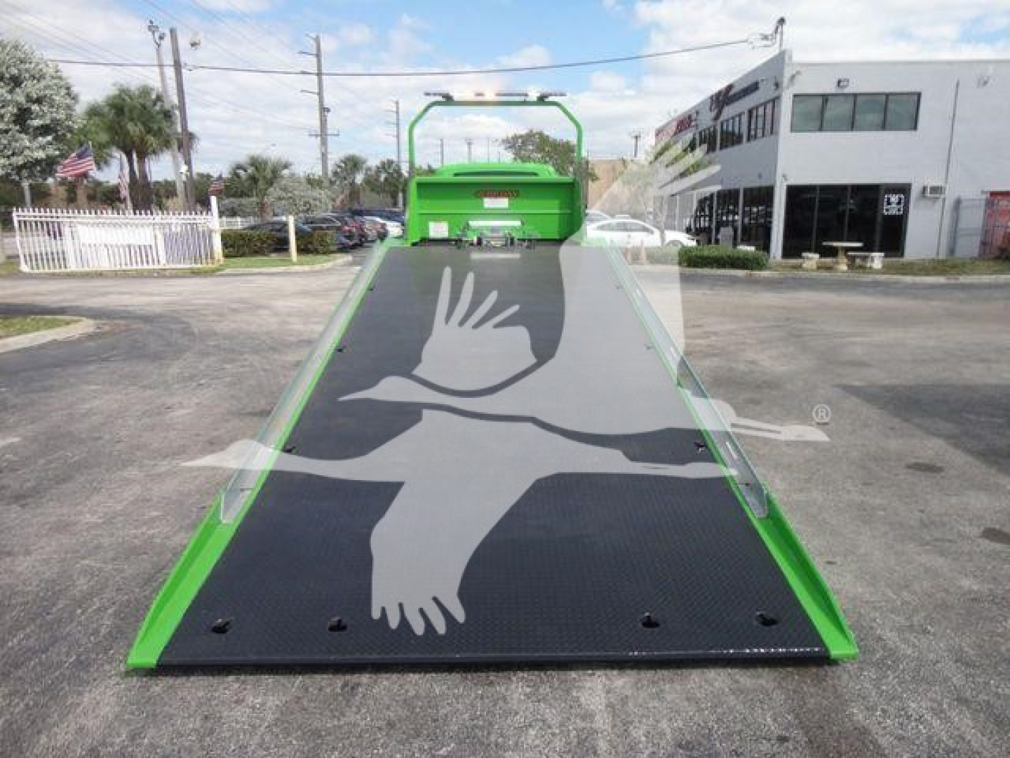 Green MV-series International rollback truck with a moving black loading ramp featuring a white bird logo and safety rails, front view in a dealership lot.