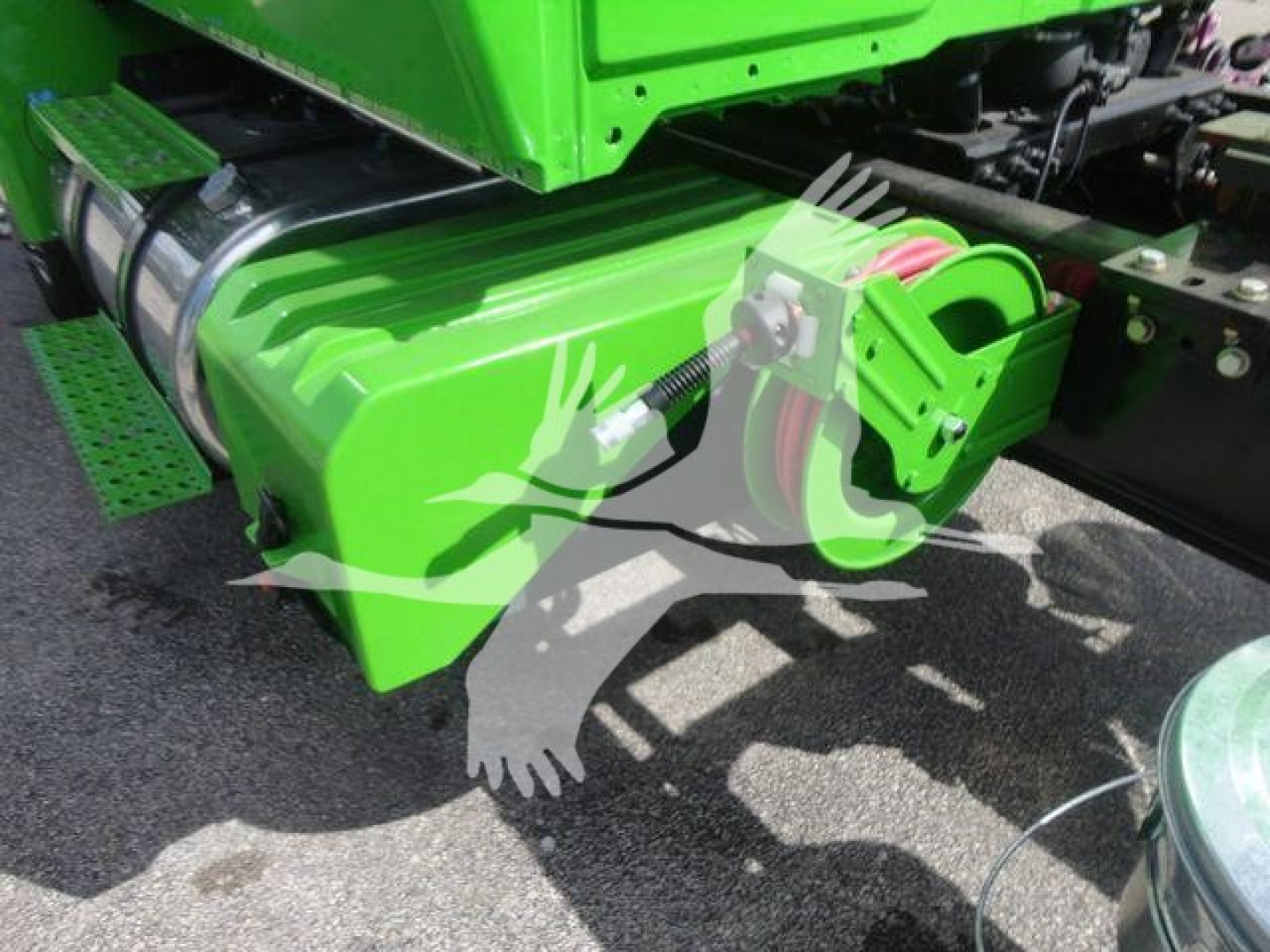Green International MV truck component showing a large rectangular green fuel or hydraulic tank with red cables and a mounting bracket; part of a rollback truck chassis.