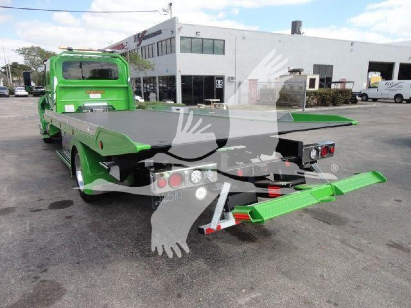 Truck bed with green rollback tow truck seen from rear left angle showing loading ramp and platform.