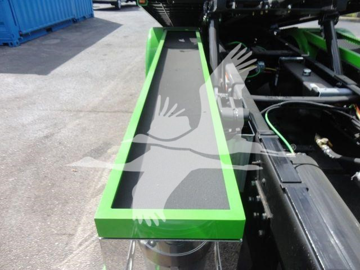 Green-framed step and black textured tread of a trailer or truck component with hydraulic lines and metal framework visible