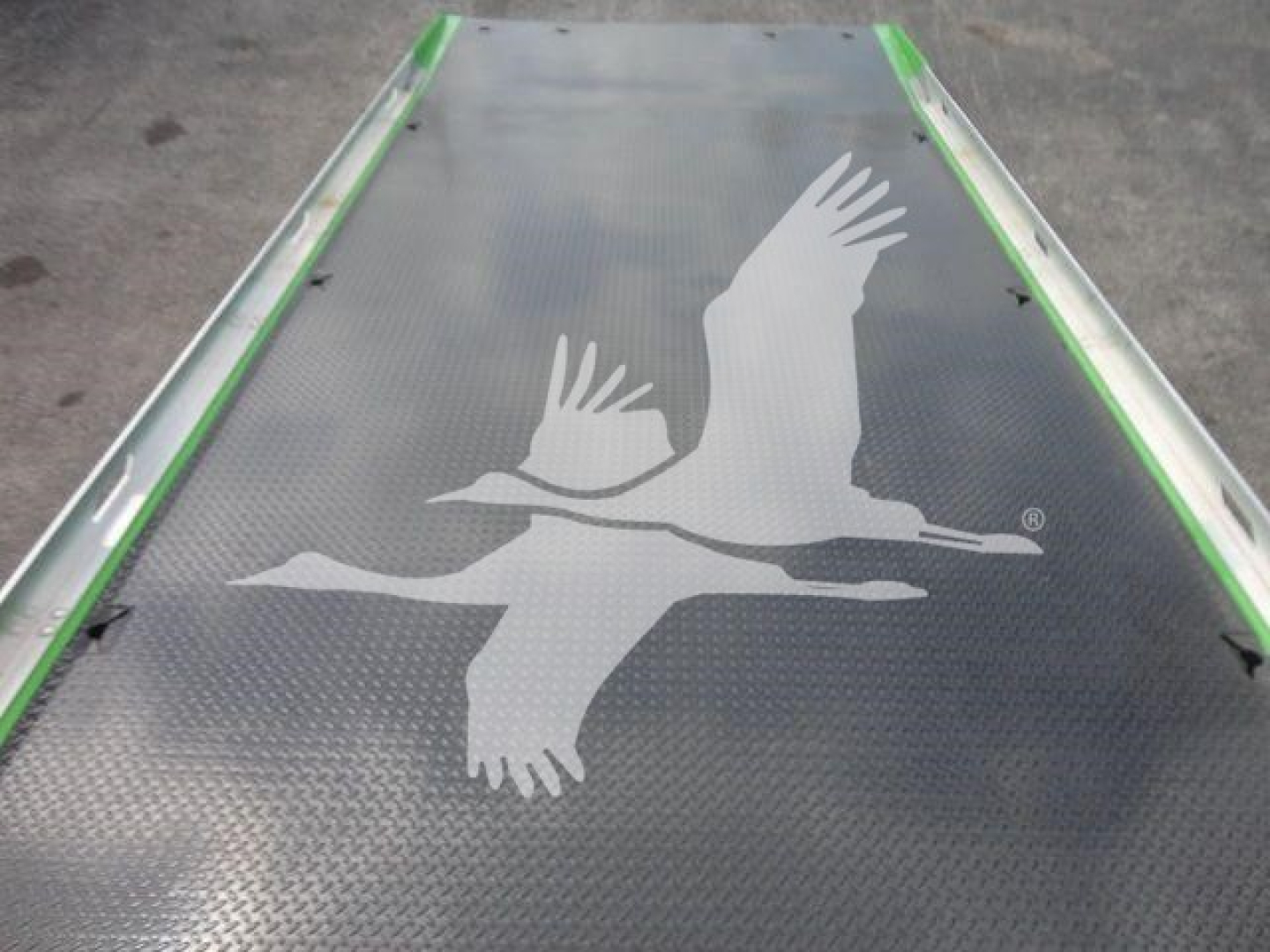 Metal truck bed or platform with a white flying bird silhouette logo on the surface, green edges, diamond plate texture.