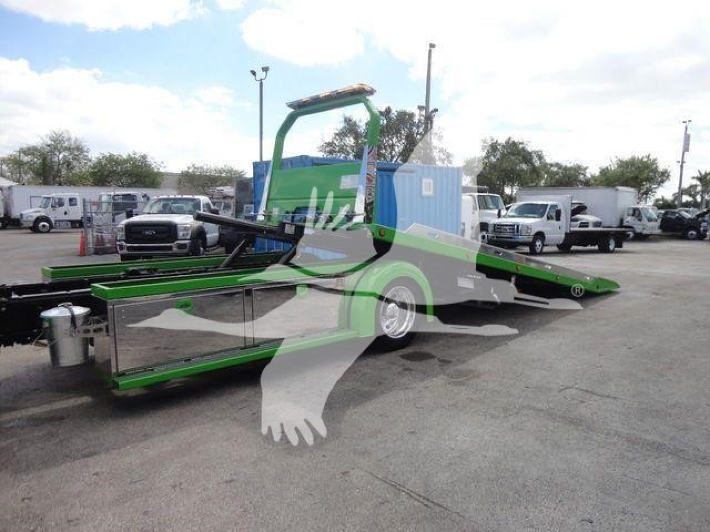 Truck with green and black rollback equipment and a blue cab unit visible in a dealership lot; MV607STEPSIDEFM stock number.
