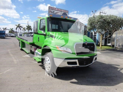 Truck in green color International MV 2027 model with rollback flatbed in a dealership lot.