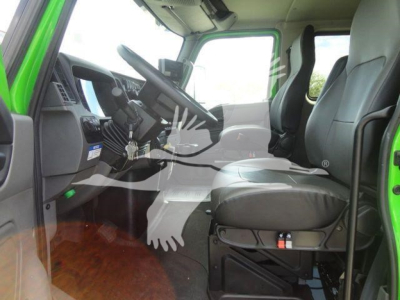 Cab interior of a green 2027 International MV truck showing driver seat, steering wheel, and dashboard with a digital display.
