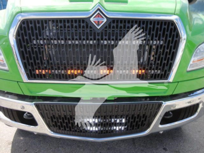 Truck front grille of a green International MV with black mesh, chrome accents, and emblem in center.