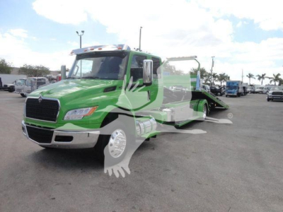 Green International MV medium-duty tow truck with flatbed in a dealership lot.