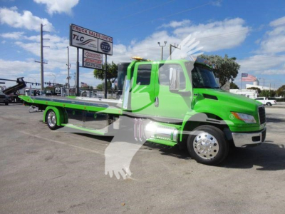 Tow truck with bright green and white livery, flatbed rollback, International MV model, side view showing extended bed and dual rear wheels.