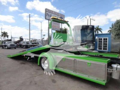 Green and silver 2027 International MV rollback tow truck side view showing flatbed and hydraulic controls with chrome storage compartments.