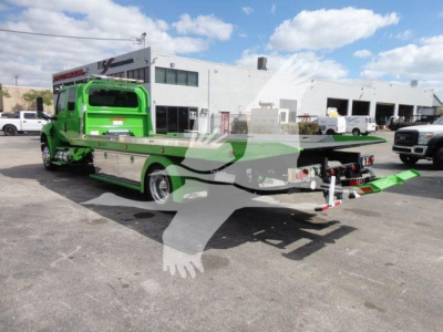 Tow truck with green cab and flatbed rollback equipment, rear view shows loading ramps and control area.