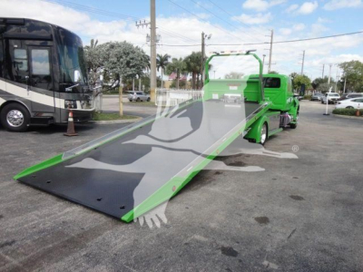  Truck with a bright green rollback tow unit and a long inclined ramp deployed in a parking lot.