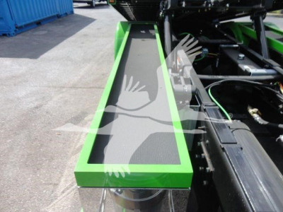 Green-framed step and black textured tread of a trailer or truck component with hydraulic lines and metal framework visible