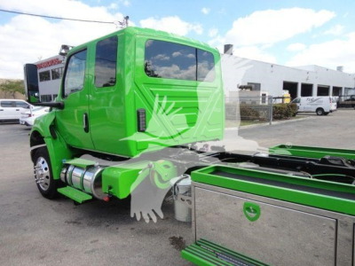 Green International MV tow truck cab and stake bed chassis side view showing cylindrical fuel tanks and chrome storage compartments.