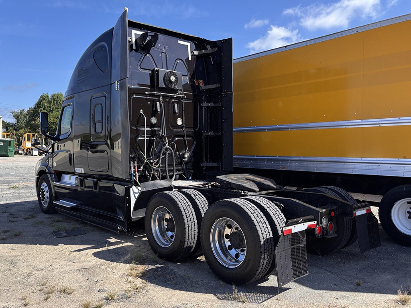 Truck cab and chassis of a 2019 Freightliner Cascadia126 in service, rear view showing exposed engine area with wiring and components.