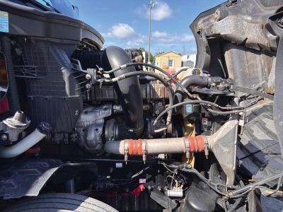 Truck engine bay view of a 2019 Freightliner Cascadia126 showing hoses, radiator, and exhaust components. Visible labels: none clearly legible; engine bay with wiring, pipes, and metal framing.