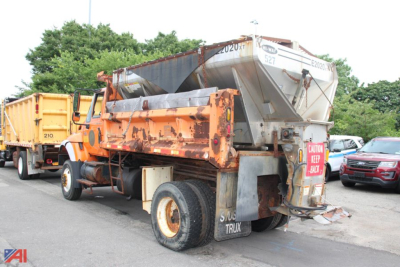 Dump truck with hopper attached, rear view showing orange bed, gray dump mechanism, and white fuel or water tank, side lettering and license plate area.