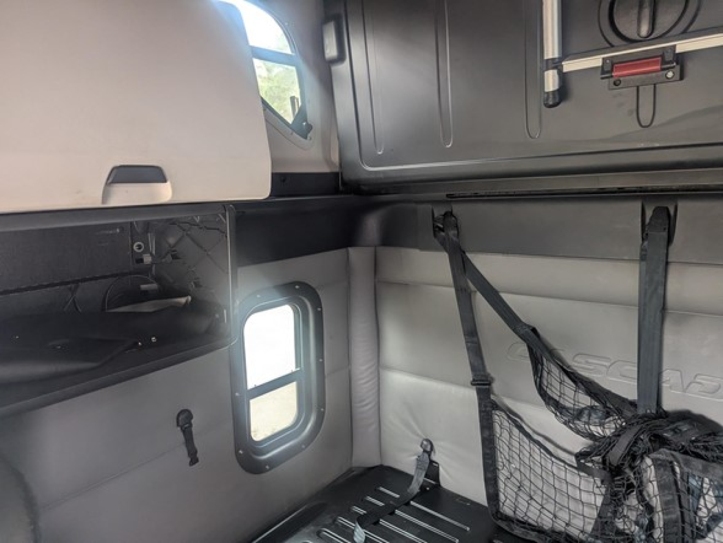 Freightliner Cascadia cab interior showing sleeper area with net storage, side window, and overhead compartments in view.