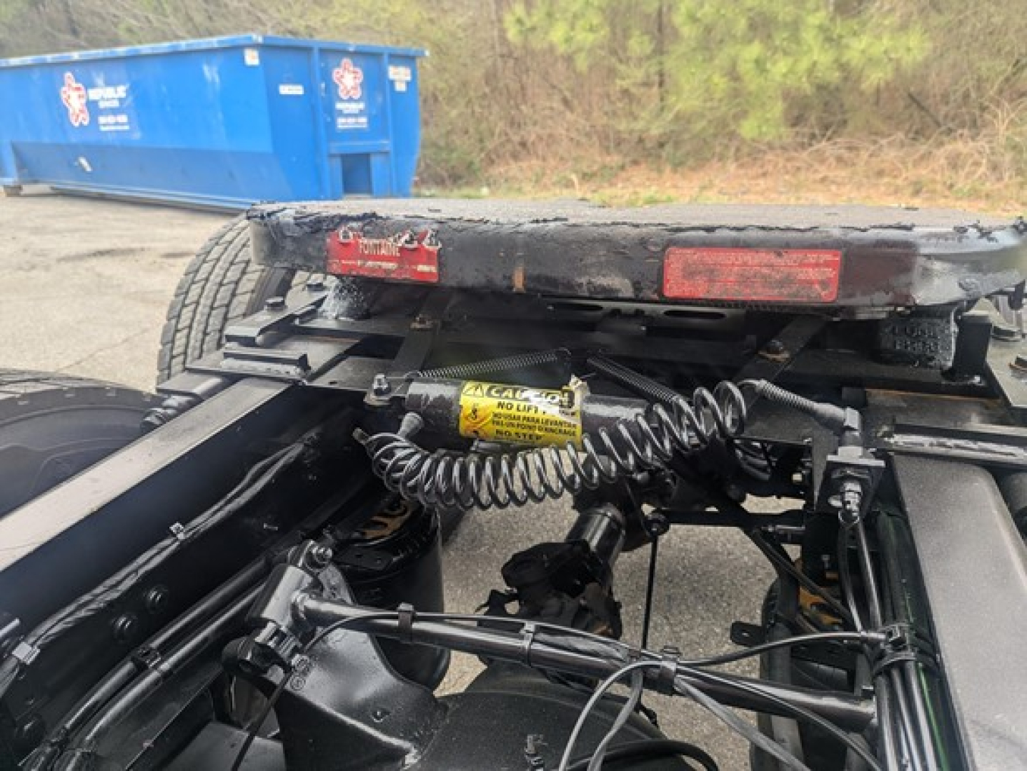 Freightliner Cascadia chassis/coupler area showing yellow warning label and coiled electrical harness with fifth-wheel plate in view.
