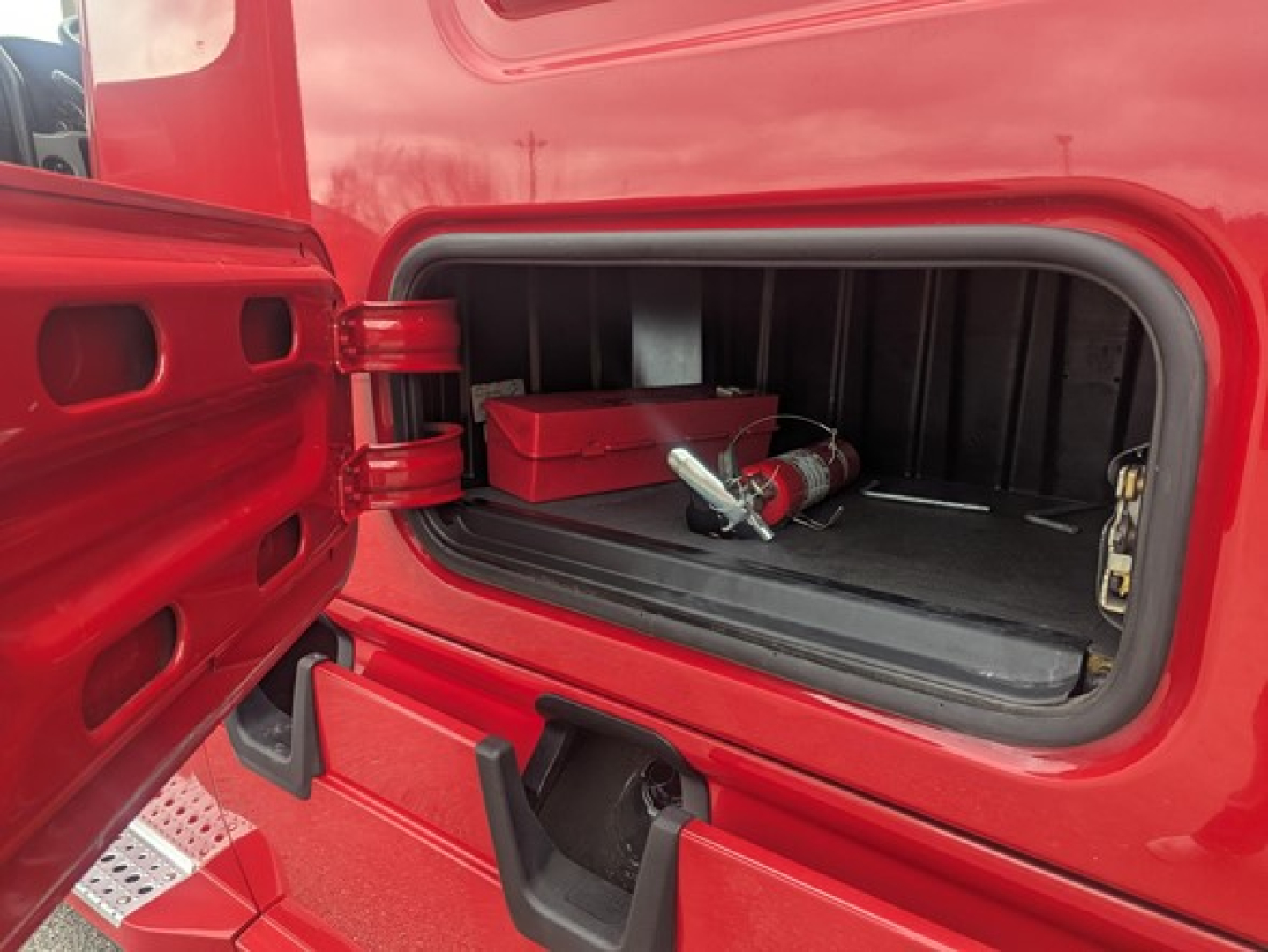 Truck cab storage area of a 2022 Freightliner Cascadia 126 showing under-bunk storage with a red toolbox and a fire extinguisher mounted in the rear compartment.