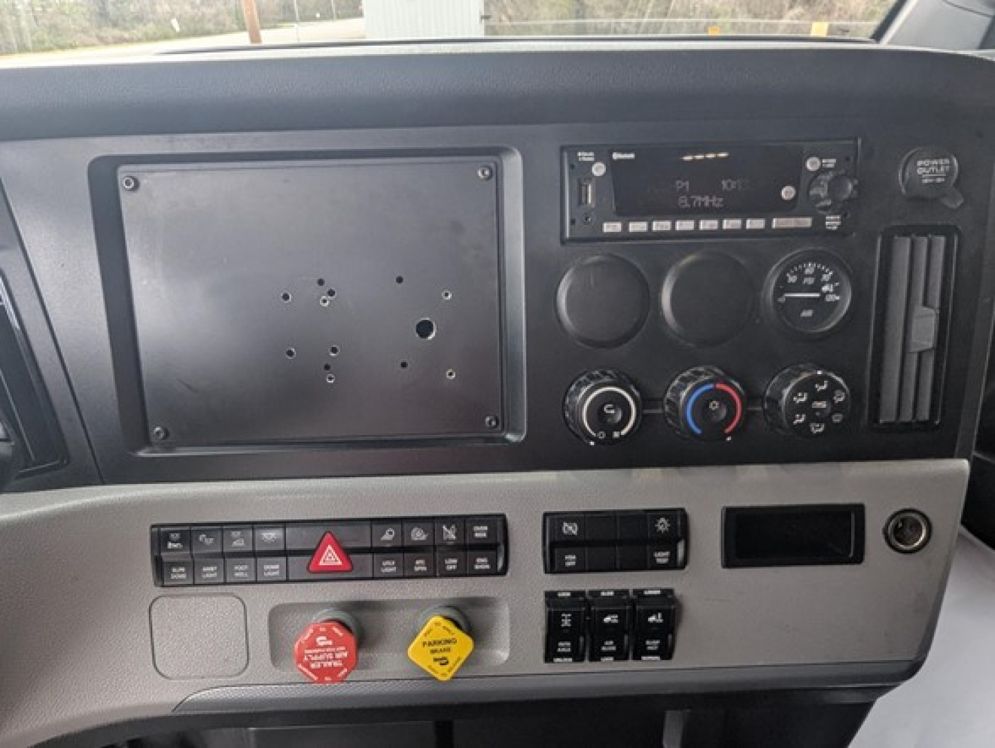 Freightliner Cascadia truck dash panel with radio, gauges, switches, and control knobs visible; blank metal plate on left side of center console.