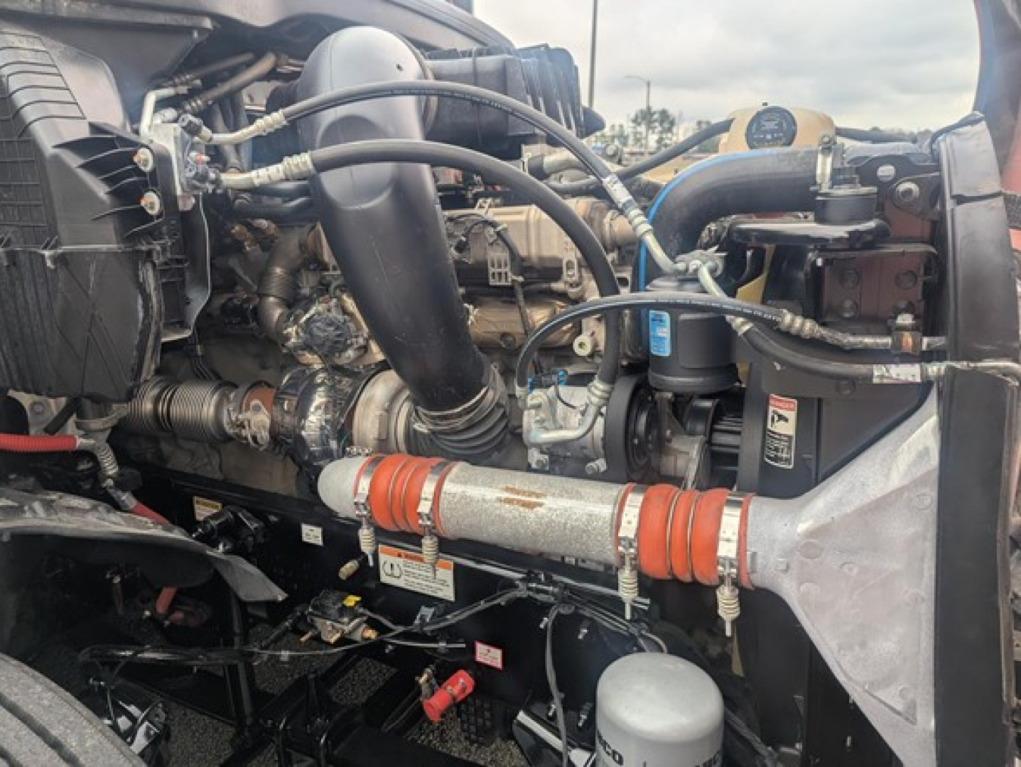Freightliner Cascadia engine bay showing turbo hoses, coolant reservoir, and orange ribbed couplers.
