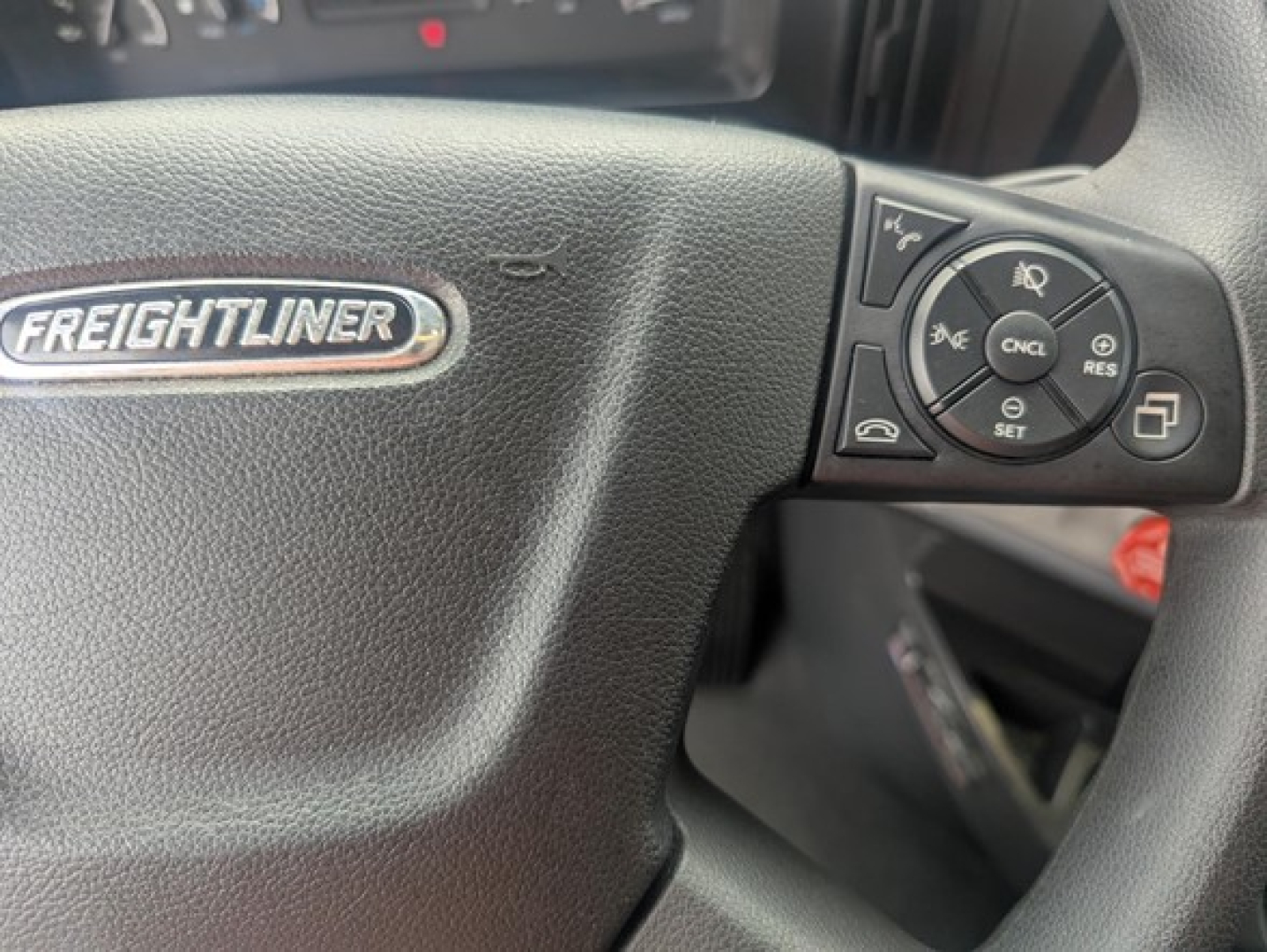 Steering wheel of a Freightliner Cascadia showing Freightliner badge and cruise control cluster on right side.