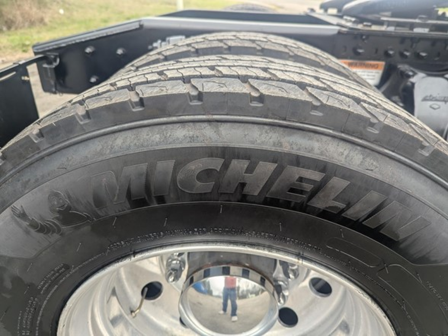 Michelin tire with visible tread on dual rear axle and chrome wheel; freightliner chassis components in background
