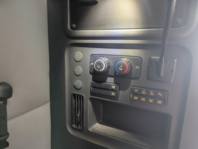Cab interior showing climate control dials, row of switches, and small storage pocket in a Freightliner Cascadia cockpit.