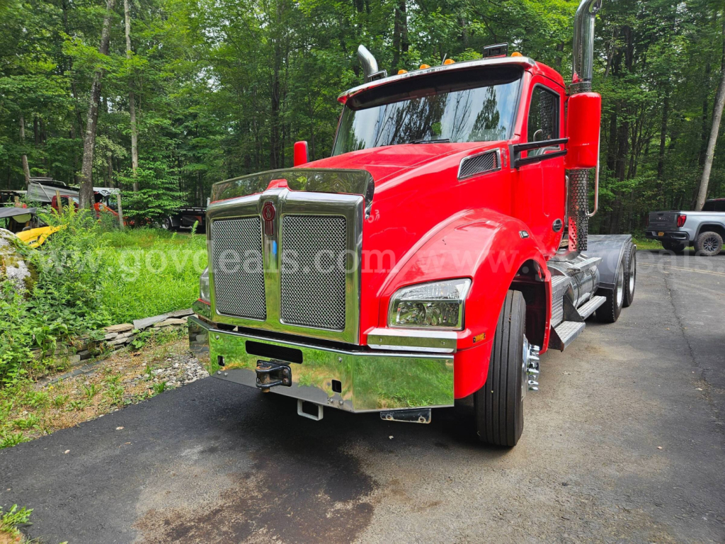 Kenworth T880 utility truck in red with chrome grille, front bumper, and large exhaust stacks; image shows front-left angle with forest background.