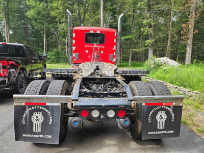 Kenworth truck rear view showing red cab, dual rear axles, mud flaps with KW logo, and chassis with fifth wheel.