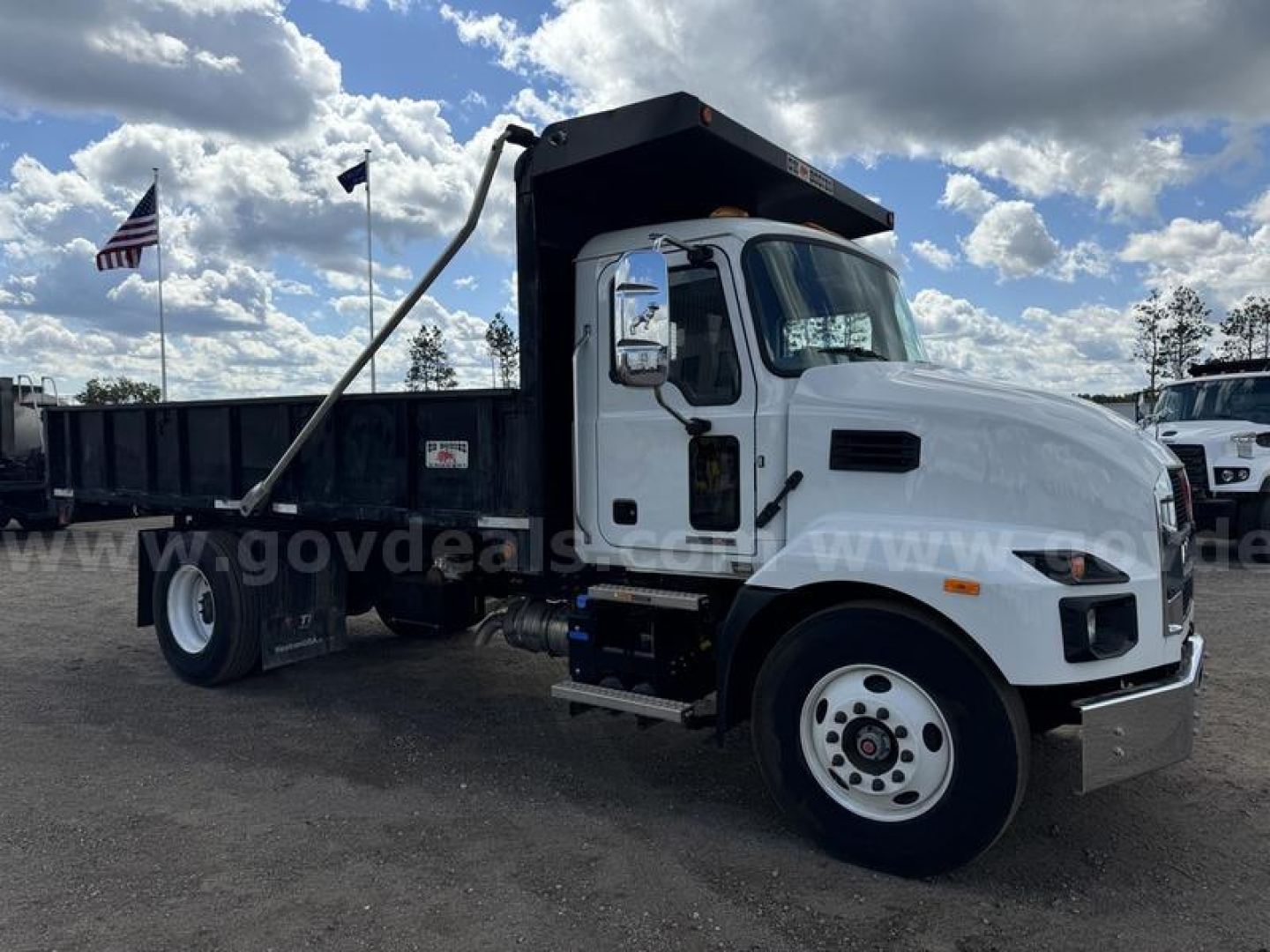 White 2024 Mack MD dump truck with black dump bed and raised side rails, front cab shows Mack emblem on grille, stock number 24329-410 not visible text on bumper, American flag in background.