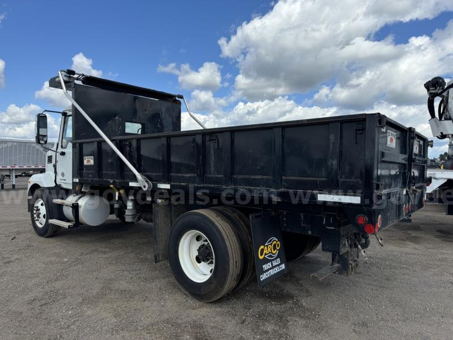 Dump truck (Mack MD) side and rear view showing dump bed and rear wheel with white rim, stock number visible, black dumpster body.