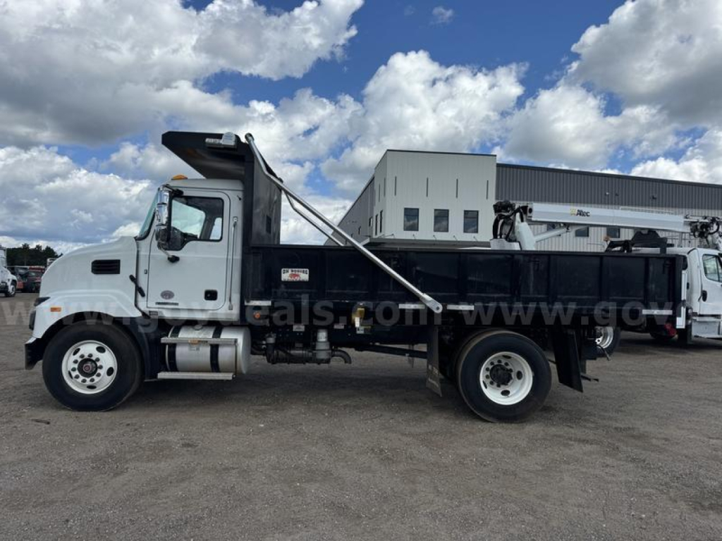 2024 Mack MD dump truck side view showing concrete cab, black dump bed, hydraulic system, and white wheels.