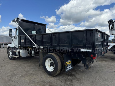 Dump truck (Mack MD) side and rear view showing dump bed and rear wheel with white rim, stock number visible, black dumpster body.