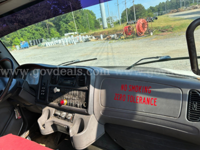 Dashboard and windshield view inside a Freightliner M2 106 dump truck showing no smoking zero tolerance sign on passenger side dash and various control panels.