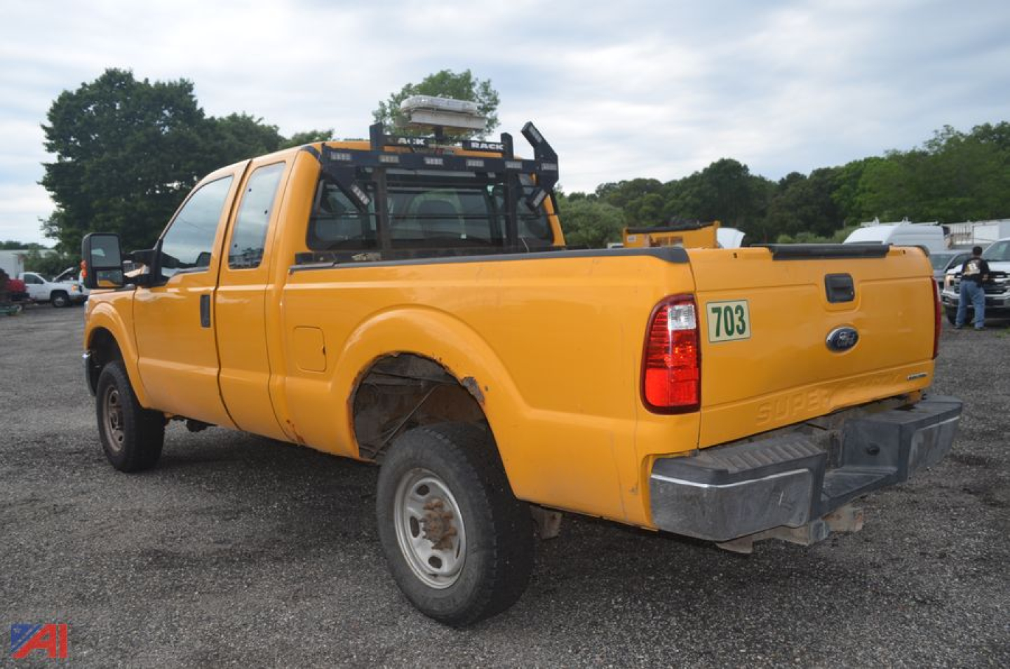 Ford F-250 Super Duty pickup truck 4x4 orange crew cab with bed rack and rear bumper, viewed from the side-rear quarter in a gravel lot.