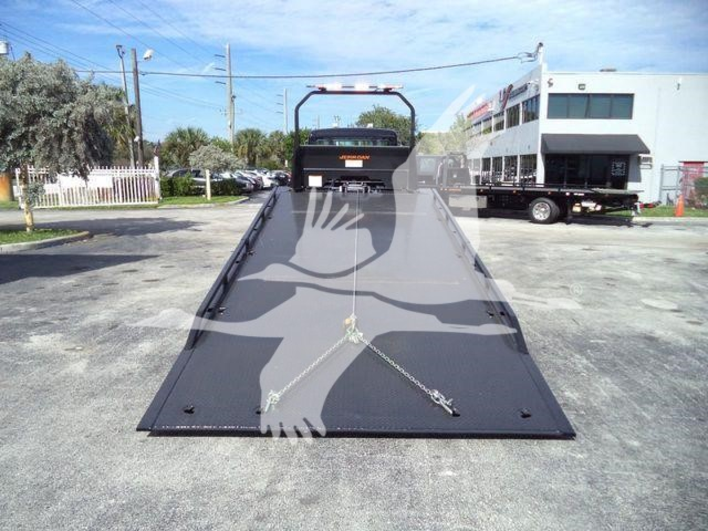 Kenworth T280 rollback tow truck flatbed viewed from rear with ramp extended and safety chains, in a dealership lot.