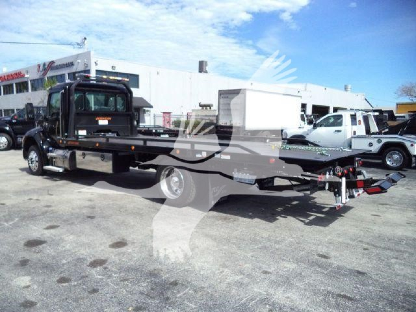 Kenworth T280 rollback truck with flatbed and lowered trailer, side view, with white cab and black flatbed; some text on equipment is not legible.