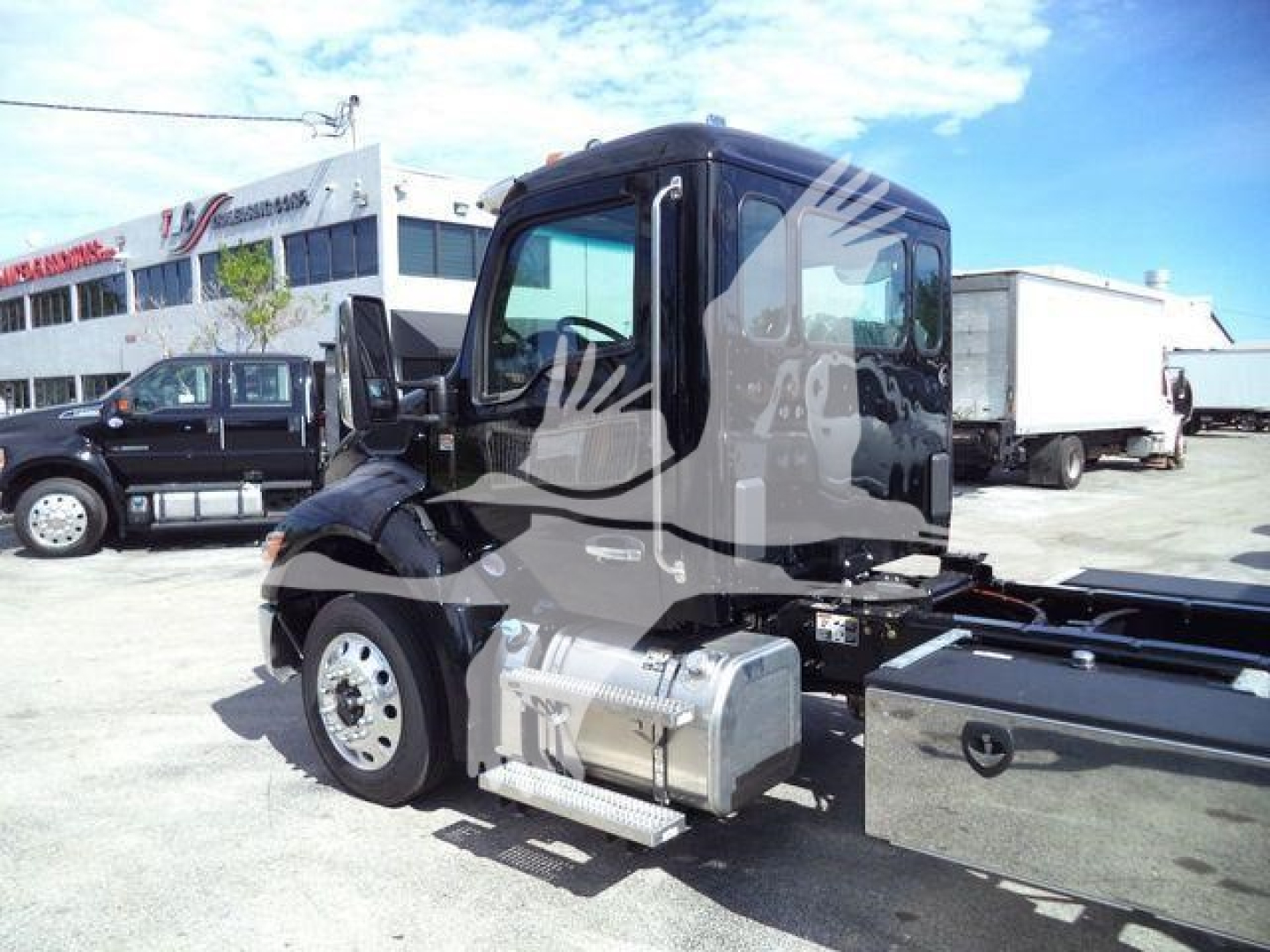 Kenworth T280 truck side view showing fuel tanks and cab, rollback in background.