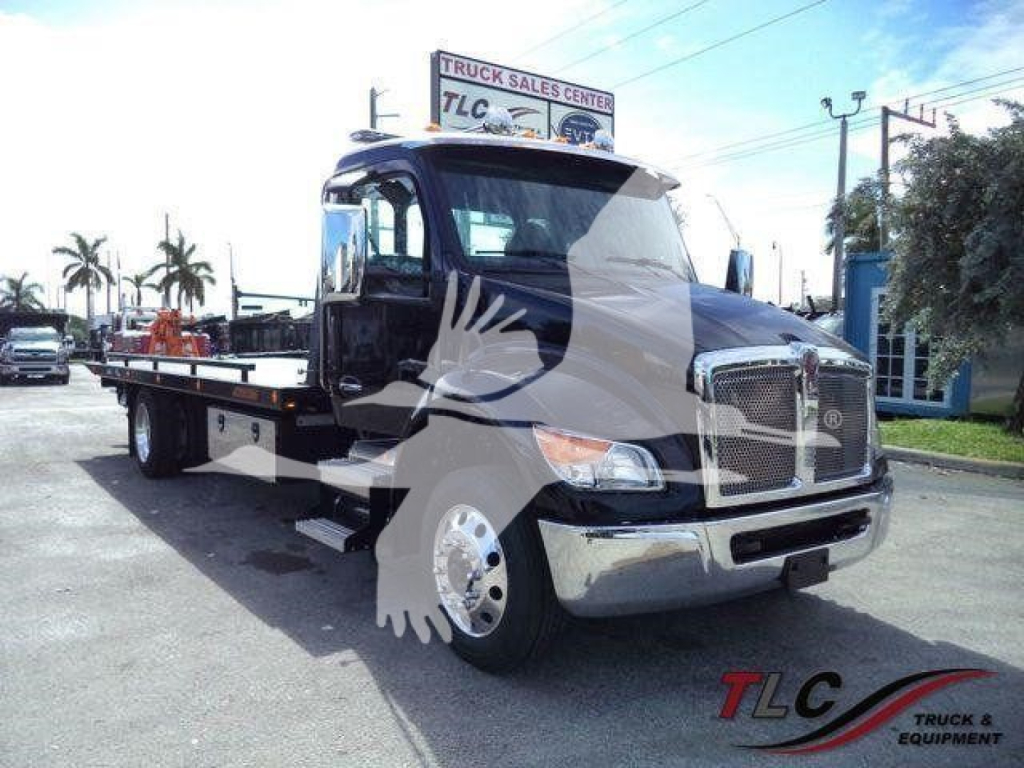 Kenworth T280 rollback truck in black with flatbed, front grille and chrome bumper, roadside with dealership sign in background.