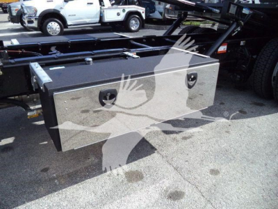 Flatbed truck toolbox mounted under a Kenworth T280 frame with black straps and two metal handles; toolbox is rectangular metallic with a textured surface.